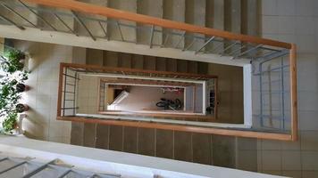 escalera moderna en edificio residencial. escalera en perspectiva. baldosas de cerámica gris. Escalera común con valla de madera marrón y escalones de concreto. vista desde arriba. foto