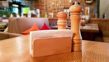 Ukraine, Kiev - September 1, 2019. A table in a cafe or restaurant. White napkins in a wooden napkin holder, spices salt and pepper on a wooden table, panoramic view photo