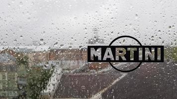 logotipo de la etiqueta engomada de martini. una marca de vermuts y vinos espumosos de fabricación italiana. gota de agua en la ventana de cristal durante la lluvia con fondo borroso de la escena de la ciudad. italia, turín - 1 de octubre de 2020. foto