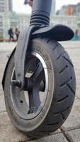 Scratched and damaged front wheel of an electric scooter on a city street against the background of paving slabs. Old e-scooter wheel. Modern technologies. Eco transport is provided for rent. photo