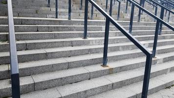 External multi-stage stone staircase. There are a lot of stairs and railings made of metal. Many steps in an urban environment, symbolic abstract background.
