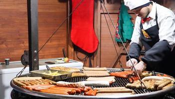 Ucrania, Kiev - 3 de enero de 2019. Un chef cocina una barbacoa a la parrilla, comida callejera, festival de comida. salchicha fresca y perritos calientes a la parrilla al aire libre. un hombre está preparando comida callejera de la cocina alemana