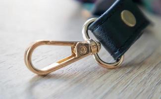 Swivel carabiner fastener with leather black bag strap on a wooden background. Metal carabiner with swivel clip or hook. Small gold fittings close-up in selective focus. photo