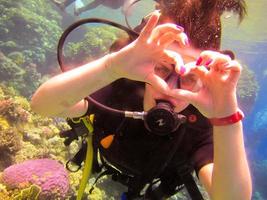 Lovely girl diver shows with a hand gesture a sign of love, a heart from fingers with a partner instructor for safe swimming under water in the Red Sea with coral reefs Egypt, Sharm El Sheikh