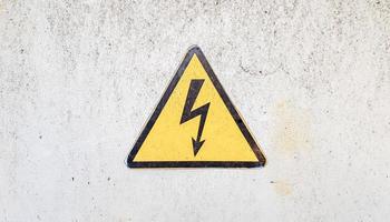 Danger sign of high voltage electricity. Yellow triangular sign with a lightning in the center. This warning is written on an old metal surface painted with gray paint. photo