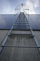 Fire escape on the industrial building above, bottom view. Stainless steel handrails, roof ladder. Detail view of stairs with safety cage. Building construction concept. photo