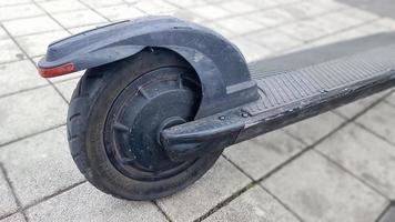 Scratched and damaged rear wheel of an electric scooter on a city street against the background of paving slabs. Old e-scooter wheel. Modern technologies. Eco transport is provided for rent. photo