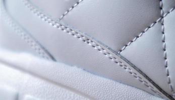 Close-up of synthetic fabric with white diamond stitching and white rubber sole. Sport shoes. Quilted fabric in white or light color, texture. photo