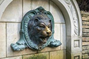 Lion head fountain on the wall. Vintage brick wall texture with lion shaped stucco. The molded face of a lion is sprayed with water. Bas-relief lion fountain. photo