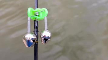Las campanas de pesca plateadas se usan en una caña de pescar mientras se pesca. señal de llamada de mordida, en la punta de la varilla. una alarma de picadura lo alertará sobre una picadura. primer plano de aparejos de pesca. foto