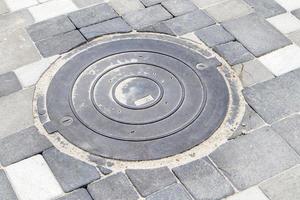 New plastic manhole cover on the sidewalk lined with gray paving slabs. The concept of sewerage, underground communications. Installation of a new sewer hatch. Construction industry. photo