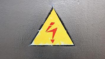 señal de seguridad amarillo y rojo sobre un fondo de metal plateado. relámpago de alto voltaje en un triángulo precaución precaución peligro electricidad muerte. foto