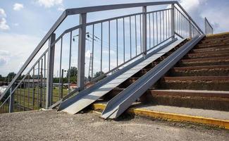 The staircase of the pedestrian crossing with traces of destruction. Two wheelchair rails. Metal railings for bicycles, wheelchairs and strollers with children. Special equipment on the stairs.