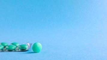 One silver blister with round green pills and one round tablet aside on a blue background. One tablet is missing from the package. conceptual medication. Copy space for your text or logo. photo