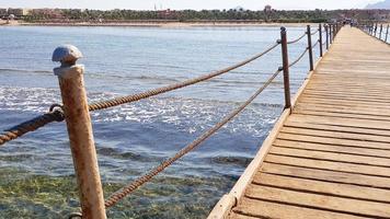 Long pontoon on the Red Sea in Egypt. Pontoon for descent into the water. Wooden bridge on the territory of the Amway Hotel in Sharm El Sheikh with metal fences and a rope over the sea with waves photo