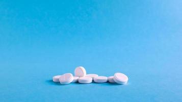 White round medical pills on a blue background. Scattered white pills on the table. The concept of medicine, pharmacy and healthcare. Copy space Empty space for text or logo. photo