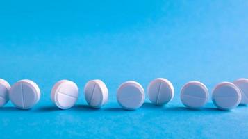 White round medical pills on a blue background. Scattered white pills on the table. The concept of medicine, pharmacy and healthcare. Copy space Empty space for text or logo. photo