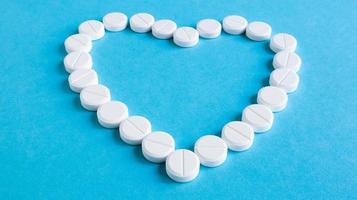 White round pills laid out in the shape of a heart on a blue background. Health symbol made of pills for therapy, treatment and healthcare concept. A medicine for lovers or potency, heart disease. photo