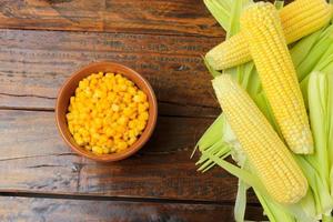 Raw corn kernels, inside ceramic bowl, next to corn on the cob on rustic wooden table. photo