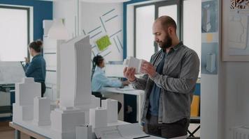 Man engineer designing blueprints plans of construction with building model in office video