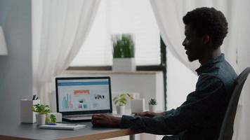 gestionnaire afro-américain travaillant à domicile, analysant des graphiques avec des ventes et des revenus video