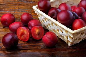 raw and fresh organic plums inside rustic fabric wooden box on rustic table photo