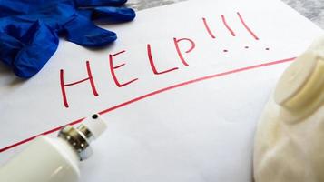 The word help is written on a white sheet with a red marker on a table with a protective mask, antiseptic, blue latex gloves. Coronavirus protection concept. photo