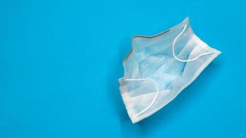 One 3-ply disposable surgical face mask with rubber pads covering the mouth and nose against a blue background. The concept of protection from bacteria, healthcare and medicine. COVID-19. copy space photo