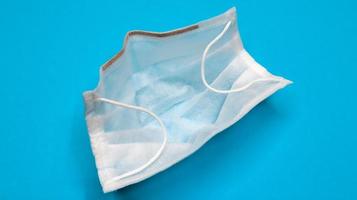 One 3-ply disposable surgical face mask with rubber grips covering mouth and nose against blue background. Protection from bacteria, healthcare and medicine concept. COVID-19. A dangerous virus. photo