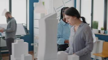 Workmates analyzing blueprints plan and building model on table, working on construction video