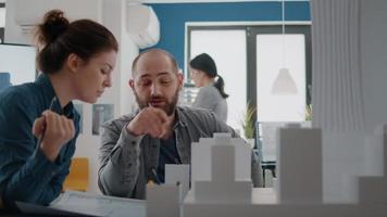 Man and woman pointing at building model to plan blueprints on paper video