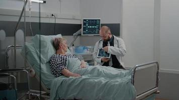 Médico explicando los resultados del escaneo de rayos X en la tableta al paciente anciano