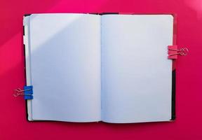 Blank notebook on a red background. Empty pages of an open book, space for writing and text. View from above. Copy space, flat lay photo