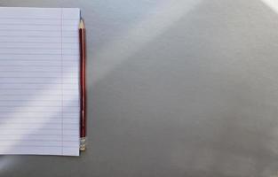 cuaderno escolar abierto con bolígrafo sobre un escritorio gris con rayos de sol desde la ventana. una hoja de cuaderno en blanco para escribir. concepto de educación. copie el espacio. vista desde arriba. endecha plana foto