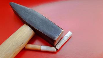 Hammer and a broken cigarette on a red background photo