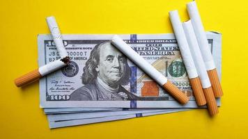 Classic cigarettes stand on one hundred US dollar bills. Cigarettes on a hundred dollar bill on a yellow background
