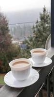 Two coffee cups on a balcony with mountain landscape in the morning. Two cups of morning coffee, standing on the side of the balcony, with a magical view of the autumn forests.