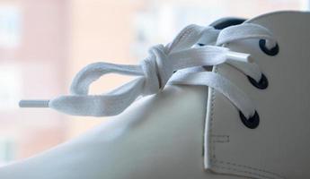 White leather sneakers lace-up shoes. White laces are tied close-up. Blurred background. Sports concept. Metal rivet for shoes as a detail or an element. Fashionable and stylish footwear. photo
