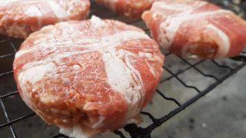 Raw meat cutlets wrapped in bacon are cooked on the grill rack. The chef prepares the grilled burger patties. Ingredients for making a hamburger. Meat lovers concept. Fast food. photo