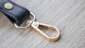 Swivel carabiner fastener with leather black bag strap on a wooden background. Metal carabiner with swivel clip or hook. Small gold fittings close-up in selective focus. photo