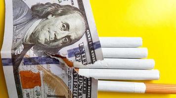 los cigarrillos clásicos se colocan en billetes de cien dólares estadounidenses. cigarrillos en un billete de cien dólares sobre un fondo amarillo