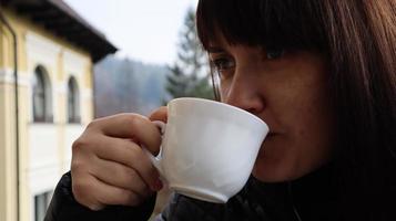 hermosa mujer con una taza de café y té disfrutando de hermosas vistas del paisaje montañoso desde el balcón del hotel. una niña feliz está desayunando en el balcón de su habitación de hotel. foto