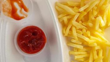 A close-up of golden orange yellow deep fries with tomato ketchup served in a foam container. Fast food takeaway. Unwanted fresh food.