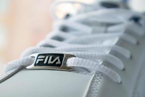 White athletic lace-up sneakers. White laces are tied close-up. Blurred background. Sports concept. Famous brand logo Fila. Fashionable and stylish footwear. Ukraine, Kiev - June 17, 2021. photo