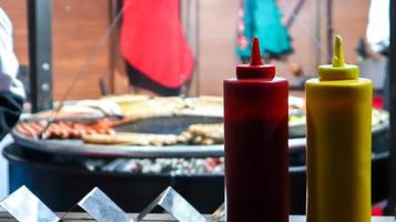 ketchup and mayonnaise in plastic tubes near a street grill in the foreground close-up with selective focus. Barbecue, street food festival. Two cans of meat sauces. Red and yellow container. photo