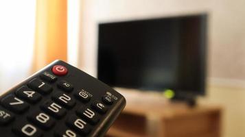 Hand holding a television remote control and surfing programs on television. watch, turn on or off the TV in the living room or bedroom on the black-screen nightstand. Copy space. photo