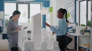 équipe d'architectes multiethniques utilisant une tablette numérique et un modèle de bâtiment pour concevoir la construction video
