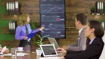 Business woman in a finance meeting pointing at graphs on tv screen