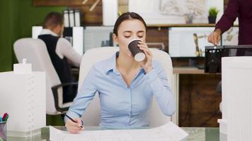 Young female architect taking a sip of coffee in architectural firm