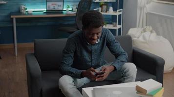 schwarzer Kerl in seinem Wohnzimmer, der das Telefon benutzt, um soziale Medien zu durchsuchen video